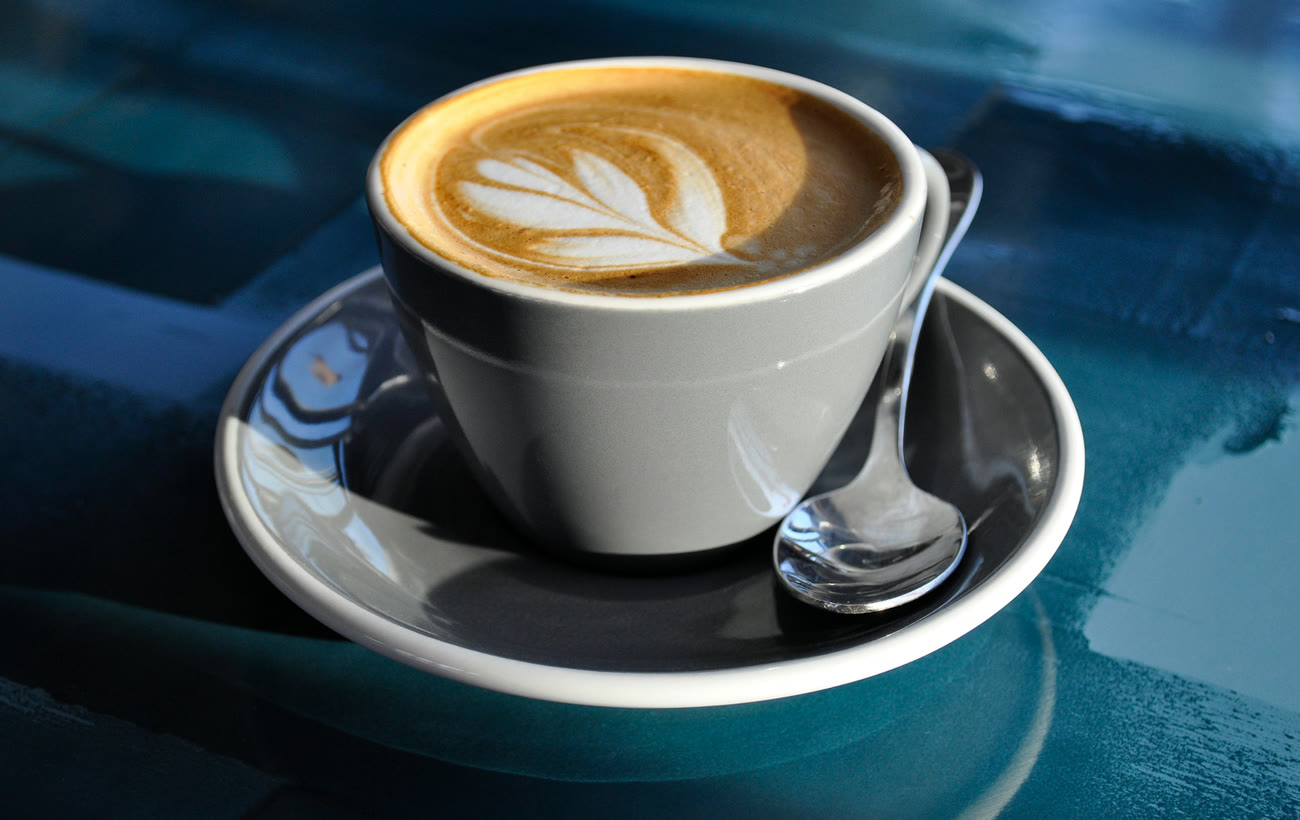 Flat white con arte de hoja sobre plato azul